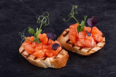 Kırmızı balıklı tost ve siyah arka planda yeşillikler.