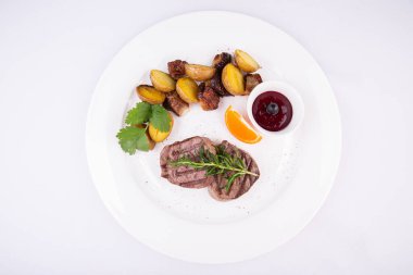 Izgara biftek, yanında patates ve kuşüzümü sosuyla servis edilir.