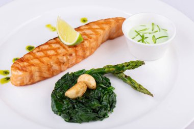 Izgara alabalık bifteği, limon, sarımsak sosu ve kuşkonmazla servis edilir.