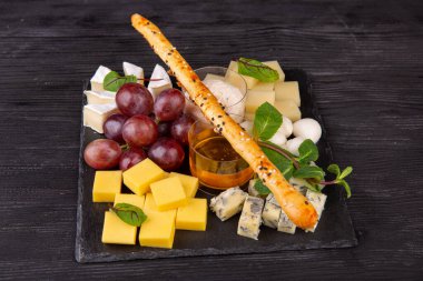 Farklı peynir çeşitleriyle servis edilen peynir tabağı, bal ve krem sosla servis edilen kırmızı üzüm ve nane.