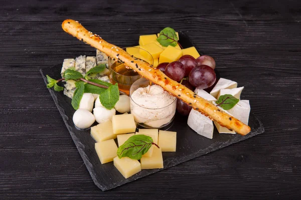 Cheese plate with different cheese varieties, served with honey and cream sauce with red grapes and mint