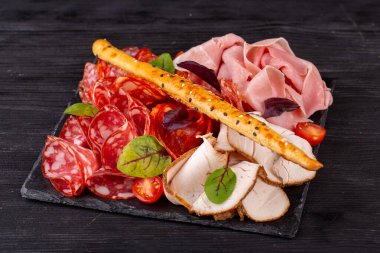 Bir sürü farklı et çeşidine sahip et tabağı, yeşillik ve vişneli domatesle servis ediliyor.