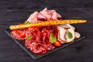 Bir sürü farklı et çeşidine sahip et tabağı, yeşillik ve vişneli domatesle servis ediliyor.