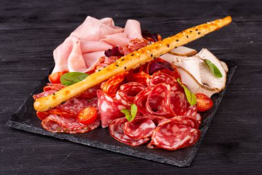 Bir sürü farklı et çeşidine sahip et tabağı, yeşillik ve vişneli domatesle servis ediliyor.