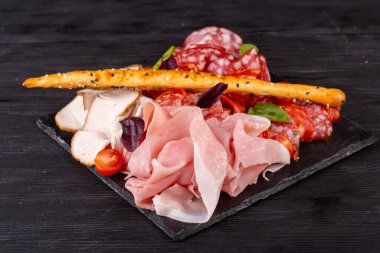 Bir sürü farklı et çeşidine sahip et tabağı, yeşillik ve vişneli domatesle servis ediliyor.