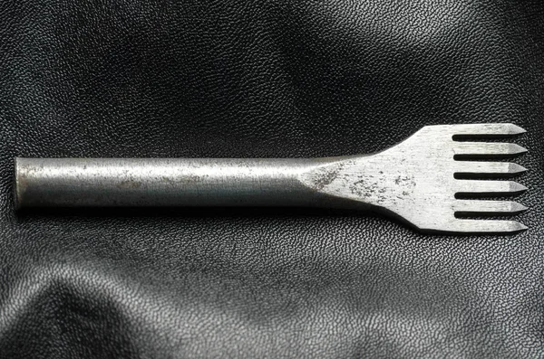 Leather punch tool. Tool for making holes in leather. Artificial leather background.