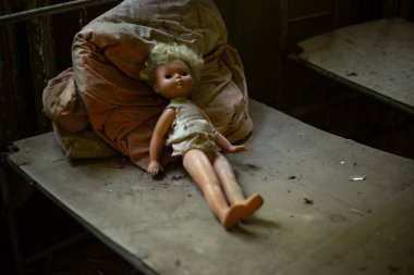 Terk edilmiş anaokulunda çocukların yatağında duran ürkütücü bir oyuncak bebek.