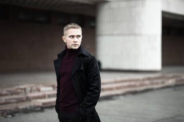 Siyah trençkotlu ciddi bir adam.