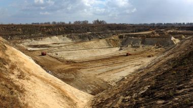 Ekskavatör bulutlu gökyüzü altında açık sanayi ocağı içine kil ayıklar