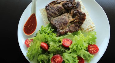 Kızarmış et ve baharatlı sos marul yaprakları ve ince ekmek ile tabakta servis