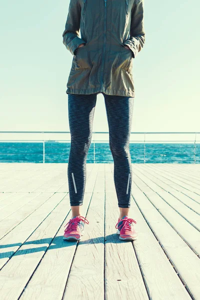 Athletic woman in a jacket and sneakers standing on a wooden dec