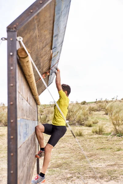 Young man climbing a wooden wall in a Spartan race — Stock Photo, Image