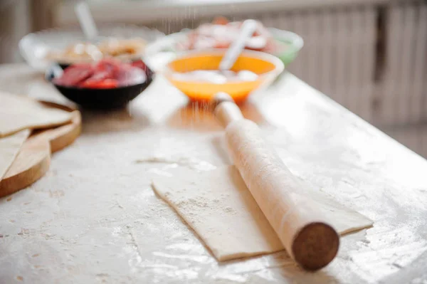 Sobre la mesa la harina de la mano del cocinero despliega la masa, los ingredientes . — Foto de Stock