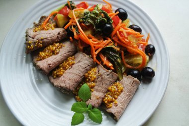 Beyaz bir tabakta, doğranmış biftek ve soslu salata dilimleri.