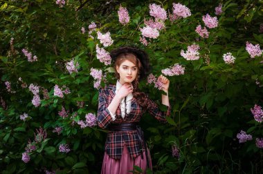 Bahçede yürüyen genç bir kadın. O, eski moda elbise ve peçeli şapka giyiyor. Ağaçlar ve yeşilliklerle çevrili.