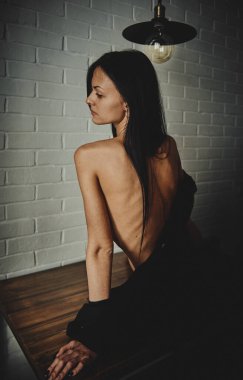 Güzel bir kız, siyah gömlekli, çıplak bir masada oturuyor.