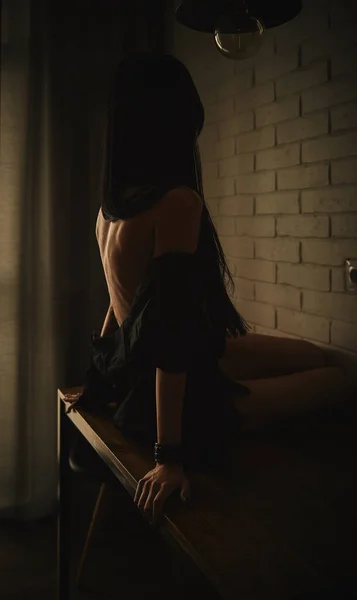 Güzel bir kız, siyah gömlekli, çıplak bir masada oturuyor.