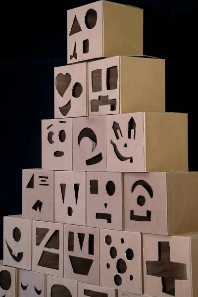 Pyramid from boxes with cuts in the form of funny persons on a black background