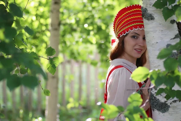 Слов'янська в традиційному одязі, ховаючись за дерев — стокове фото