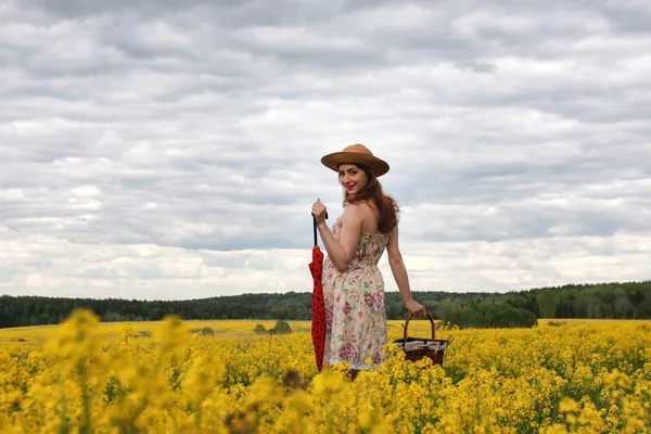 Ragazza in un campo di fiori con un ombrello e un cappello — Foto Stock