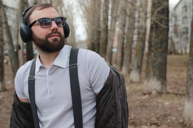 Sakallı ve kulaklıklı bir adam parkta.