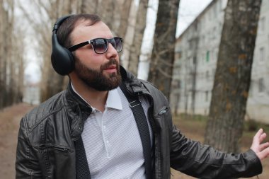 Sakallı ve kulaklıklı bir adam parkta.