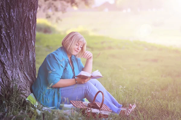 Жінка в парку на заході сонця з книгою — стокове фото