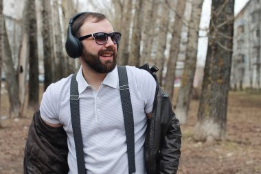 Sakallı ve kulaklıklı bir adam parkta.