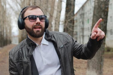 Sakallı ve kulaklıklı bir adam parkta.