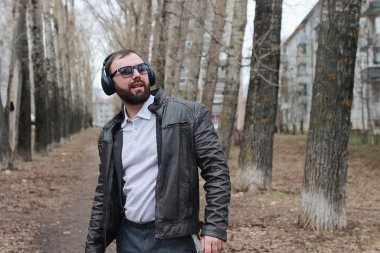 Sakallı ve kulaklıklı bir adam parkta.