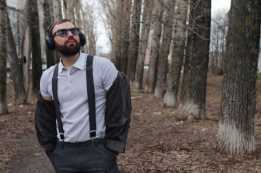 Sakallı ve kulaklıklı bir adam parkta.