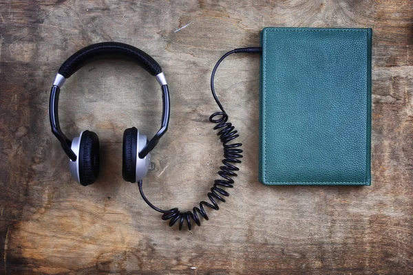 Fones de ouvido audiobook e livro em mesa de madeira — Fotografia de Stock