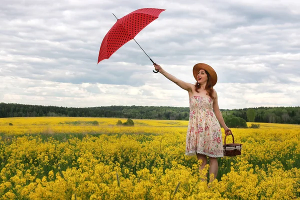Kız bir şemsiye ve bir şapka çiçeklerle dolu bir alanda — Stok fotoğraf