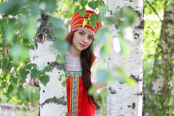 Слов'янська в традиційному одязі, ховаючись за дерев — стокове фото