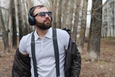 Sakallı ve kulaklıklı bir adam parkta.