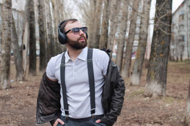 Sakallı ve kulaklıklı bir adam parkta.