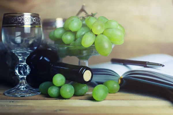 Wooden table with wine bottle book and grape — Stock Photo, Image