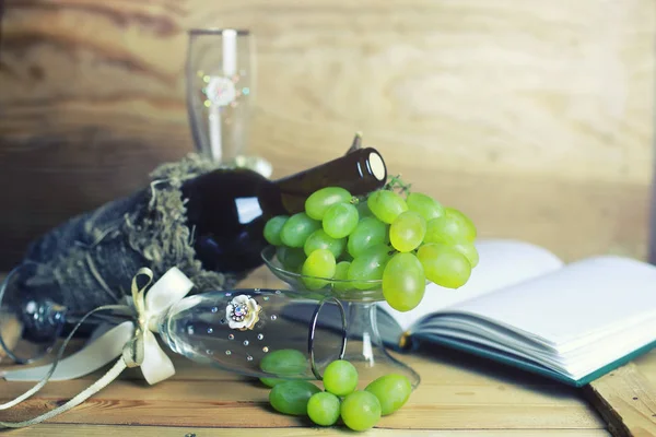 Wooden table with wine bottle book and grape — Stock Photo, Image