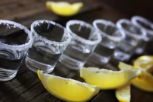 Pilha de tequila com sal e limão em um fundo de madeira — Fotografia de Stock