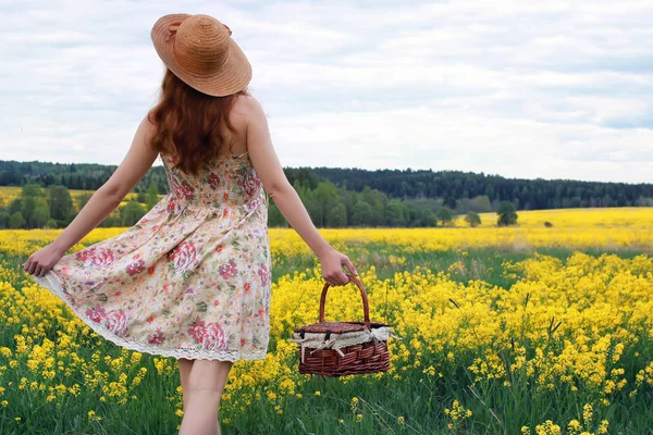 Ragazza in un campo di fiori con cesto e un cappello — Foto Stock