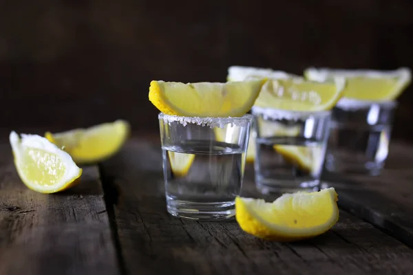 Pilha de tequila com sal e limão em um fundo de madeira — Fotografia de Stock