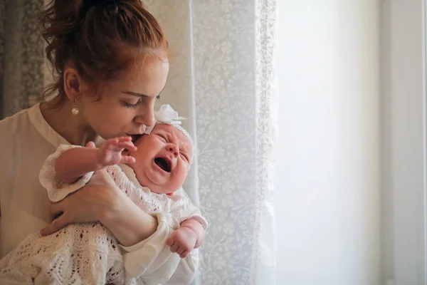 Ung mamma och nyfödd baby i famnen står vid fönstret — Stockfoto