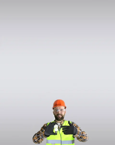 Werknemer in een helm en beschermende kleding met een gloeilamp in — Stockfoto