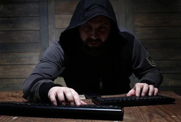 Hacker en la capucha negra en una habitación con paredes de madera —  Fotos de Stock
