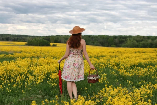 Ragazza in un campo di fiori con un ombrello e un cappello — Foto Stock