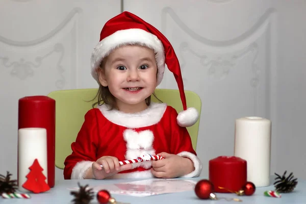 Criança em um terno de Papai Noel escrevendo uma carta com desejos de — Fotografia de Stock