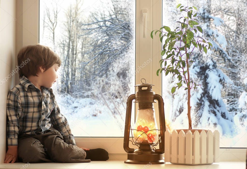 boy sitting on a white window sill and looks out the window