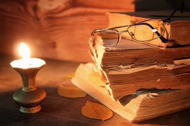 ahşap bir masa üzerinde eski püskü kitap mum ve gözlük ışıklı