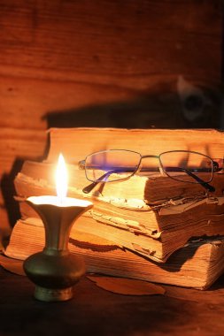 ahşap bir masa üzerinde eski püskü kitap mum ve gözlük ışıklı