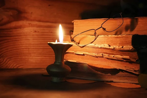 ahşap bir masa üzerinde eski püskü kitap mum ve gözlük ışıklı